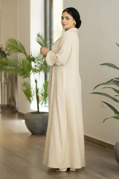 Beige maxi dress with pleated front and long sleeves, made from Ketan fabric.