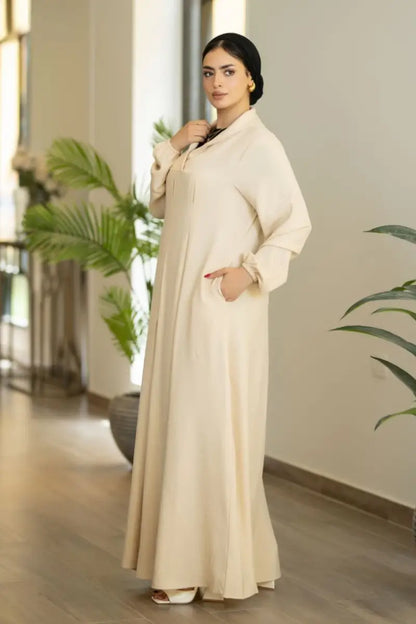 Beige maxi dress with pleated front and long sleeves, made from Ketan fabric.