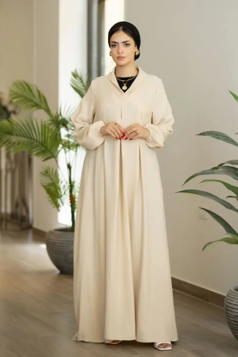 Beige maxi dress with pleated front and long sleeves, made from Ketan fabric.