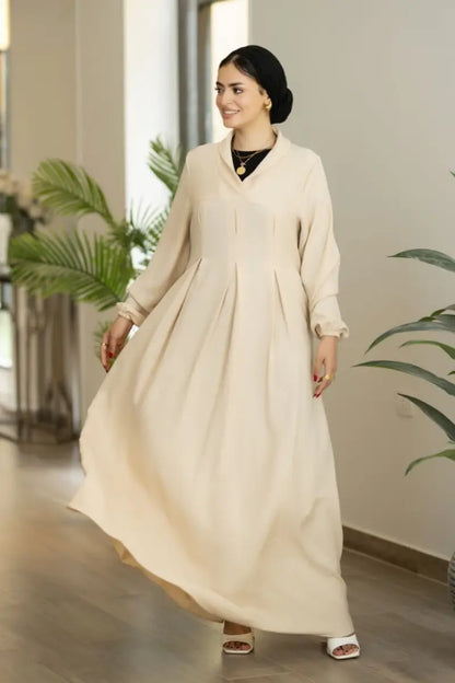 Beige maxi dress with pleated front and long sleeves, made from Ketan fabric.